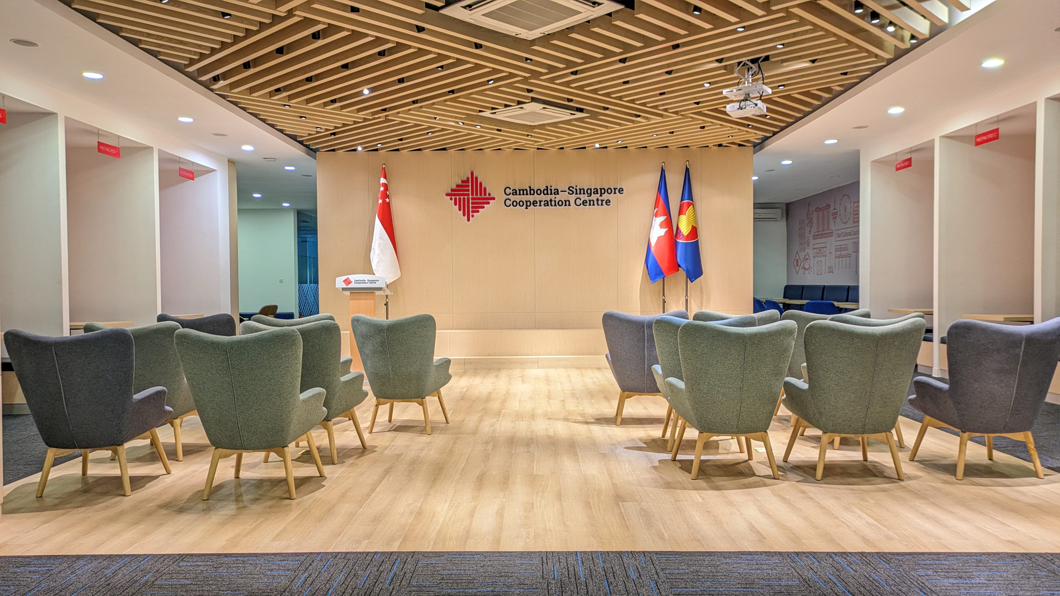 Meeting room with the flags of Cambodia and Singapore, and gray and green wingback chairs.